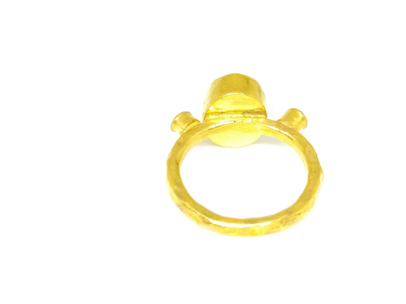 May include: A gold ring with a round, smooth stone set in the centre. The ring has a textured band and is made of hammered metal.