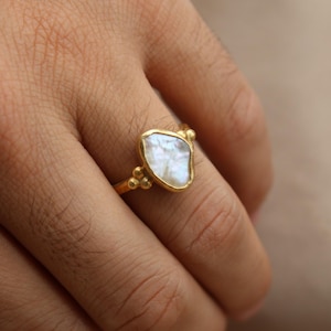 May include: A gold ring with a white, irregular shaped gemstone. The ring has small gold beads around the gemstone.