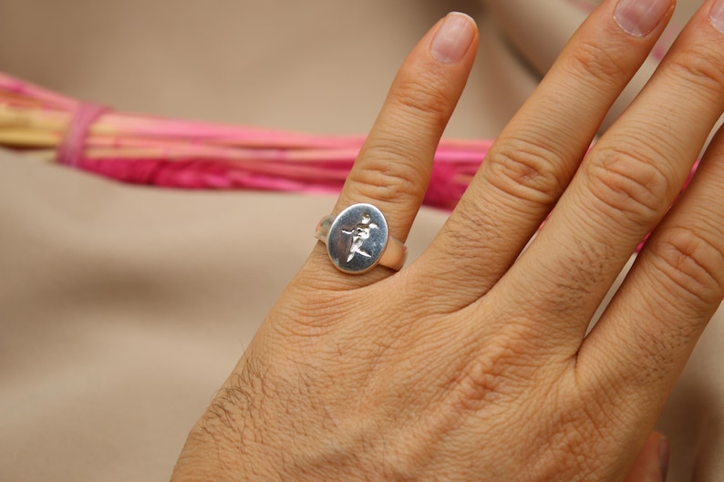 以下が含まれることがあります： 花柄の楕円形のデザインが施されたシルバーリング。リングは手の指先につけられています。