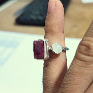 K&ouml;nnte beinhalten: Ein silberner Ring mit einem gro&szlig;en, rechteckigen, dunkelroten Edelstein und einem kleineren, runden, wei&szlig;en Edelstein.