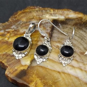 K&ouml;nnte beinhalten: Ein schwarzer Onyx-Anh&auml;nger und Ohrringe mit silbernen Filigrandetails. Anh&auml;nger und Ohrringe haben runde schwarze Onyx-Steine.