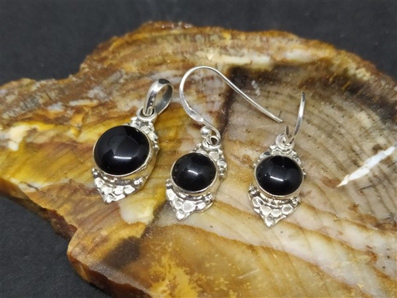 K&ouml;nnte beinhalten: Ein schwarzer Onyx-Anh&auml;nger und Ohrringe mit silbernen Filigrandetails. Anh&auml;nger und Ohrringe haben runde schwarze Onyx-Steine.
