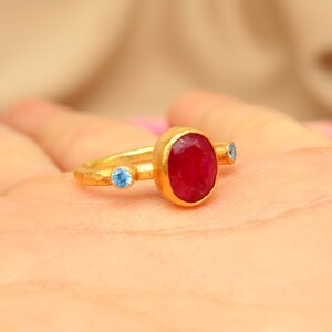 K&ouml;nnte beinhalten: Ein goldener Ring mit einem gro&szlig;en roten Edelstein und zwei kleineren blauen Edelsteinen.