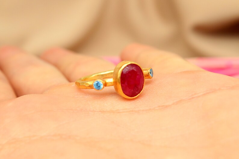 K&ouml;nnte beinhalten: Ein goldener Ring mit einem gro&szlig;en roten Edelstein und zwei kleineren blauen Edelsteinen.