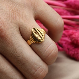 Op de afbeelding: Een gouden ring met een getextureerd ovaalvormig ontwerp. De ring wordt aan een vinger gedragen.