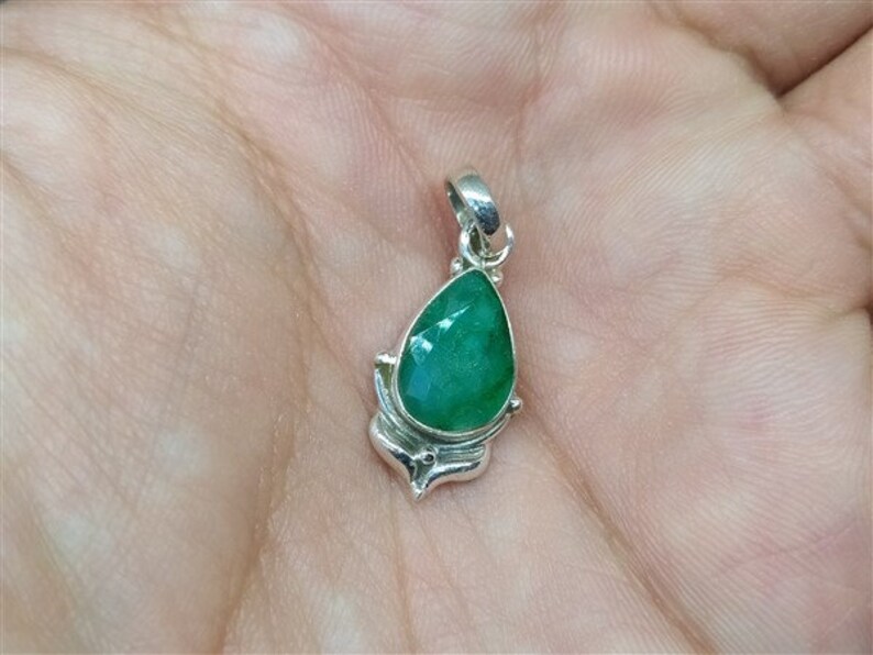 Pu&ograve; includere: Ciondolo in argento con una pietra preziosa verde smeraldo sfaccettata a forma di pera. Il ciondolo ha un'incastonatura decorativa in argento e un'asola per una catena. La pietra misura circa 1,9 cm di lunghezza.