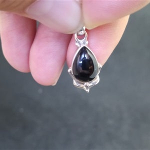 May include: A silver pendant featuring a black teardrop-shaped gemstone.