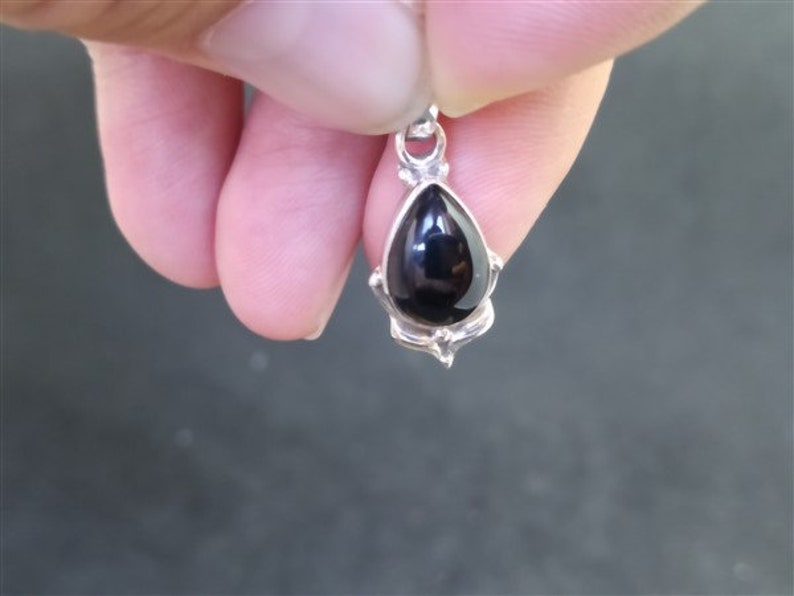 May include: A silver pendant featuring a black teardrop-shaped gemstone.