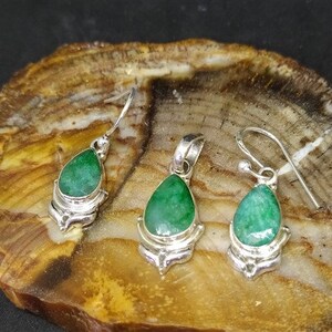 Pu&ograve; includere: Un set di gioielli con un ciondolo e orecchini abbinati. Ogni pezzo ha una gemma verde vibrante a forma di goccia incastonata in metallo color argento. Gli orecchini hanno un design a gancio, mentre il ciondolo ha un anello per una catena.