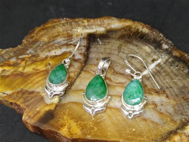 Pu&ograve; includere: Un set di gioielli con un ciondolo e orecchini abbinati. Ogni pezzo ha una gemma verde vibrante a forma di goccia incastonata in metallo color argento. Gli orecchini hanno un design a gancio, mentre il ciondolo ha un anello per una catena.