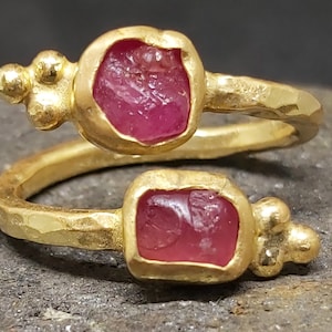Può includere: Un anello d'oro con due pietre preziose rosa incastonate in oro martellato. L'anello è un gioiello unico ed elegante.