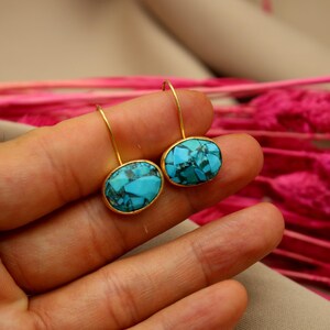 May include: A pair of gold earrings with oval turquoise stones. The stones have a blue and green marbled pattern.
