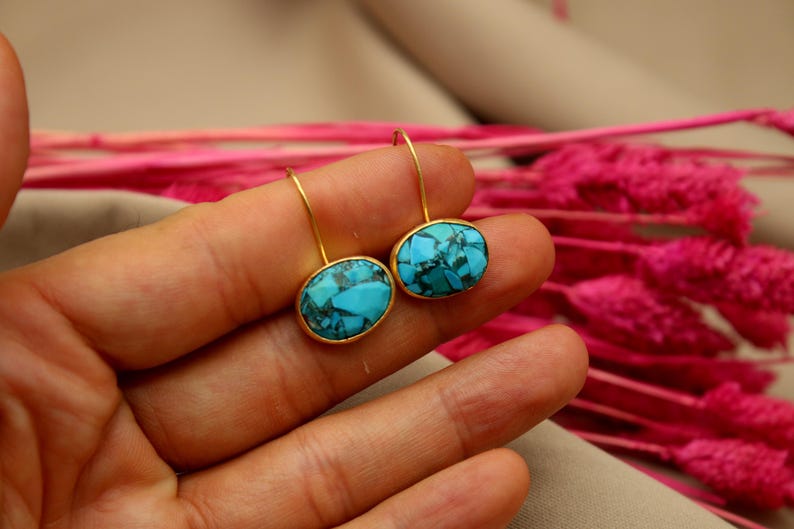 May include: A pair of gold earrings with oval turquoise stones. The stones have a blue and green marbled pattern.