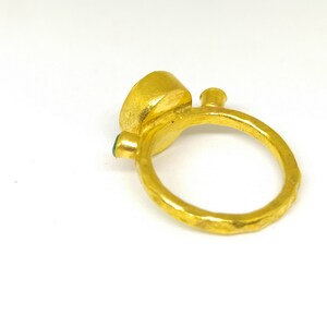 May include: A gold ring featuring a large, round, green gemstone set in the centre. The ring has a textured band and a smaller green gemstone on the side.