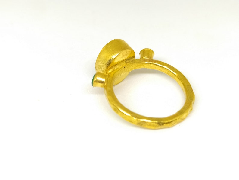 May include: A gold ring featuring a large, round, green gemstone set in the centre. The ring has a textured band and a smaller green gemstone on the side.