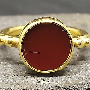 May include: A gold ring with a red carnelian stone set in a bezel setting. The ring has a beaded band.