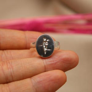 以下が含まれることがあります： 花を持っている人の詳細なデザインが施された、楕円形のセッティングのシルバーリングです。