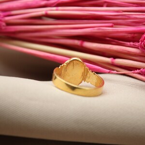 Op de afbeelding: Een gouden ring met een ovale steen in het midden. De ring ligt op een witte stoffen achtergrond.