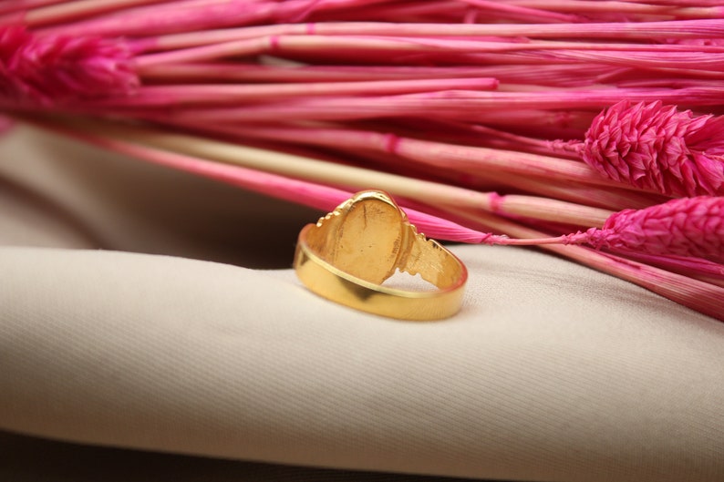 Op de afbeelding: Een gouden ring met een ovale steen in het midden. De ring ligt op een witte stoffen achtergrond.