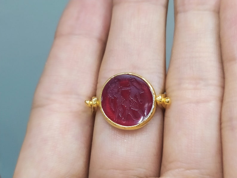 Peut inclure: Une bague en or avec un cam&eacute;e rouge orn&eacute; d'un motif sculpt&eacute;. Le cam&eacute;e est serti dans une b&eacute;li&egrave;re ronde et la bague a une bande simple.