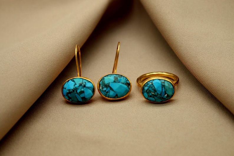 May include: A set of turquoise gemstone jewelry featuring a ring and a pair of earrings. The gold-toned metal settings are accented with oval-shaped turquoise stones.