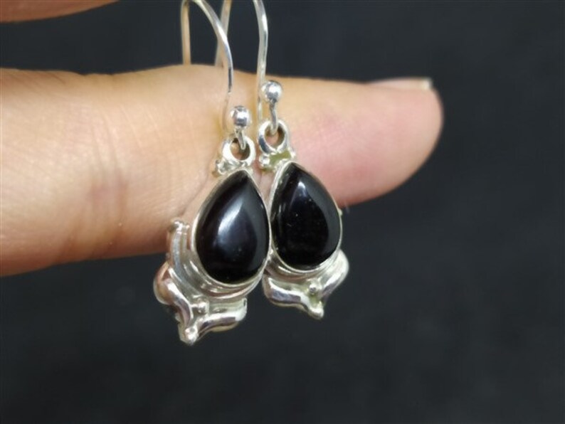 May include: A pair of silver dangle earrings with black teardrop-shaped stones.