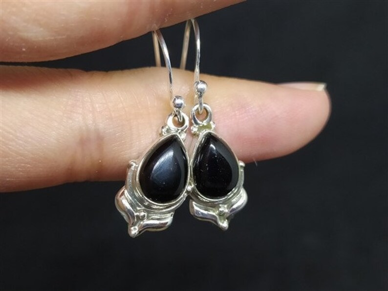 May include: A pair of silver dangle earrings with black teardrop-shaped stones.