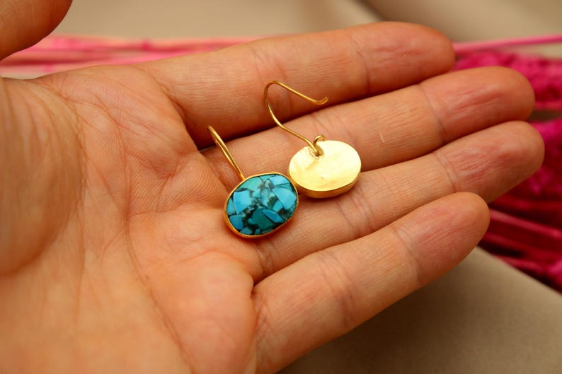May include: A pair of gold earrings with turquoise stones. The earrings are oval shaped and have a simple design.