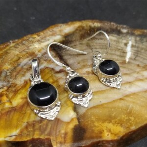 K&ouml;nnte beinhalten: Ein Set aus silbernen Ohrringen und einem Anh&auml;nger mit schwarzen Onyx-Steinen. Jedes St&uuml;ck hat ein detailliertes Silberdesign um den Stein herum.