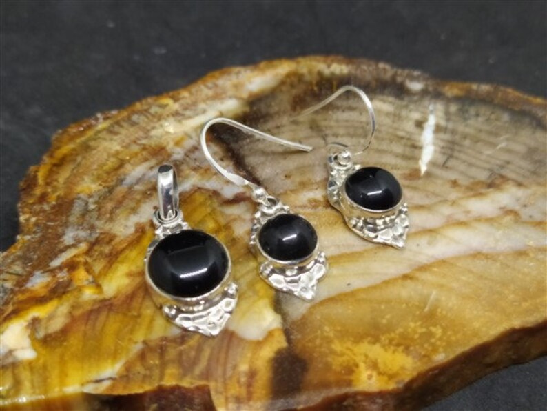 K&ouml;nnte beinhalten: Ein Set aus silbernen Ohrringen und einem Anh&auml;nger mit schwarzen Onyx-Steinen. Jedes St&uuml;ck hat ein detailliertes Silberdesign um den Stein herum.