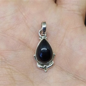May include: A silver pendant featuring a black gemstone in the shape of a teardrop. The pendant has an ornate design around the gemstone.
