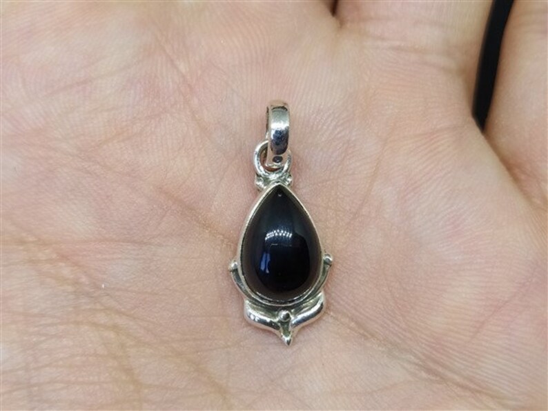 May include: A silver pendant featuring a black gemstone in the shape of a teardrop. The pendant has an ornate design around the gemstone.