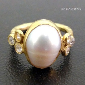May include: A gold ring with a large white pearl and smaller clear gemstones set in the band.