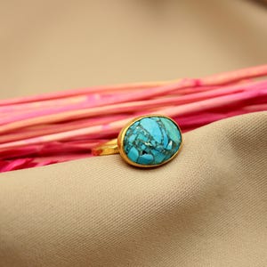 May include: A gold ring with a large oval turquoise stone. The stone has a blue and green marbled pattern.