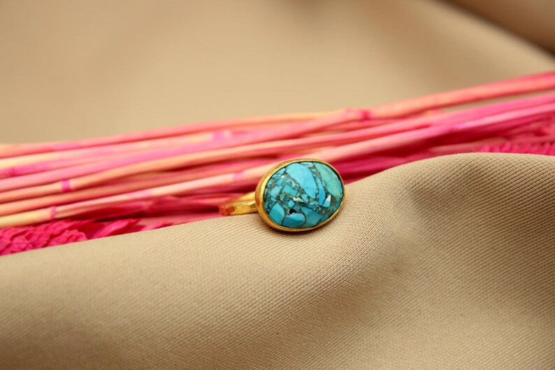 May include: A gold ring with a large oval turquoise stone. The stone has a blue and green marbled pattern.