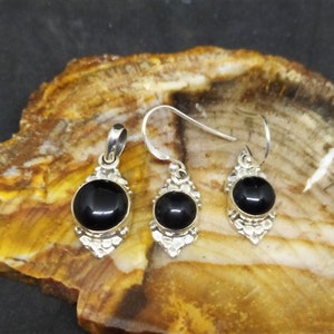 K&ouml;nnte beinhalten: Ein Set aus silbernen Ohrringen und einem Anh&auml;nger mit schwarzen Onyx-Steinen. Die Ohrringe und der Anh&auml;nger haben aufwendige silberne Designs.
