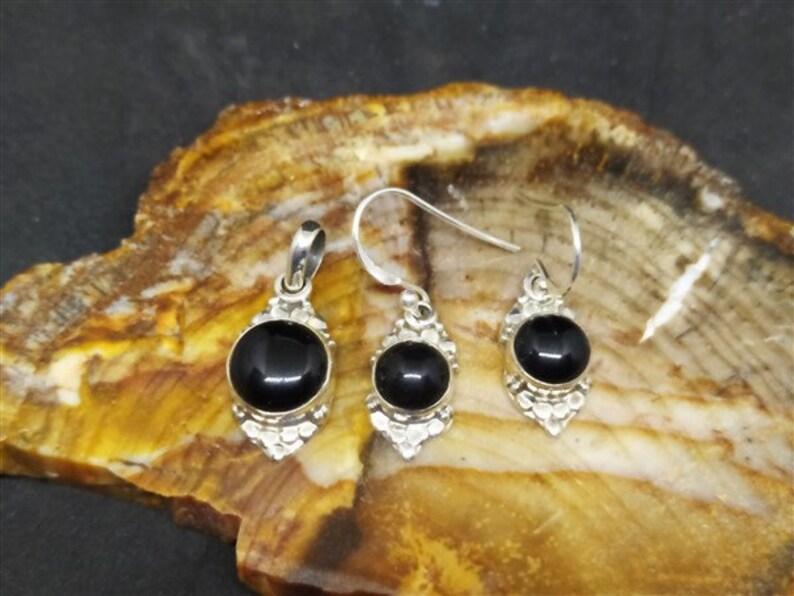 K&ouml;nnte beinhalten: Ein Set aus silbernen Ohrringen und einem Anh&auml;nger mit schwarzen Onyx-Steinen. Die Ohrringe und der Anh&auml;nger haben aufwendige silberne Designs.