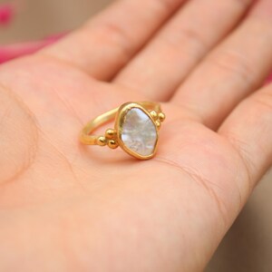 May include: A gold ring with a white, irregular shaped gemstone. The ring has small gold beads around the gemstone.
