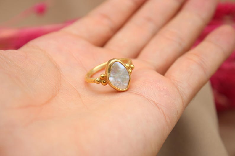 May include: A gold ring with a white, irregular shaped gemstone. The ring has small gold beads around the gemstone.