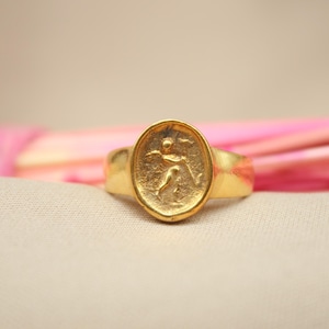 May include: A gold ring with an oval-shaped design featuring a raised image of a person in a running pose.