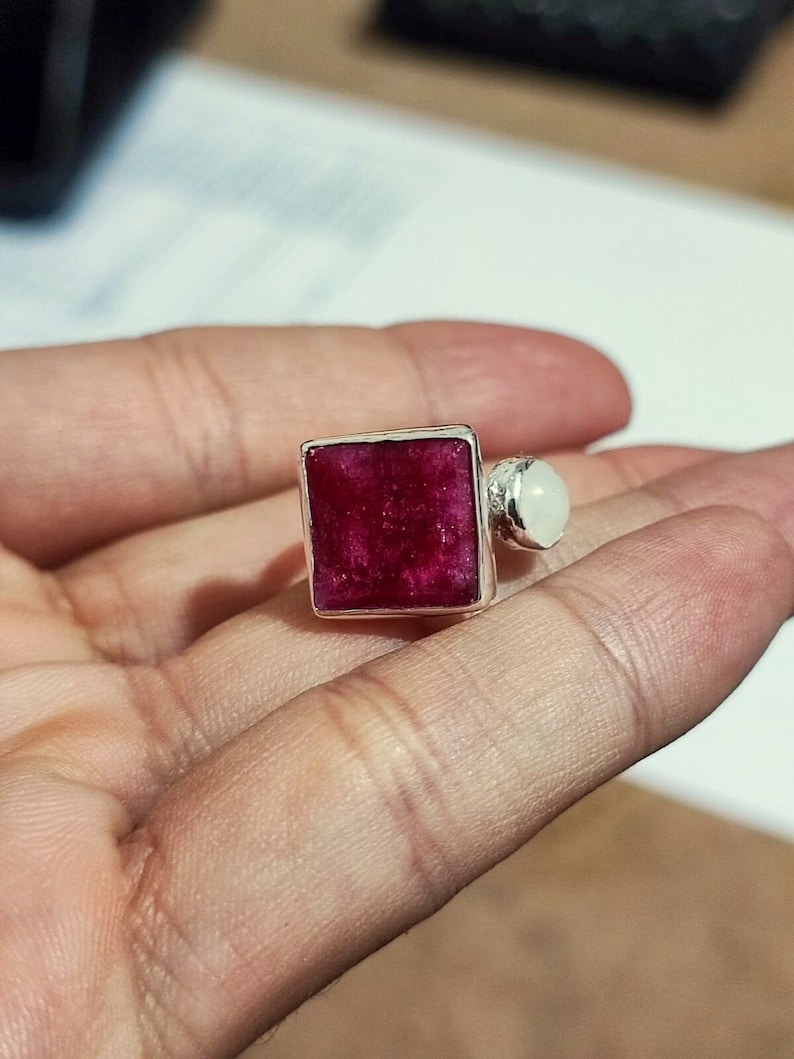 K&ouml;nnte beinhalten: Ein silberner Ring mit einem quadratischen roten Edelstein und einem kleineren wei&szlig;en Edelstein an der Seite.