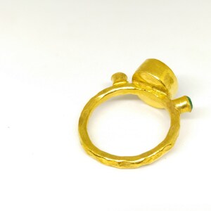 May include: A gold ring with a textured band and a large round gemstone. The ring has a smaller green gemstone on the side.