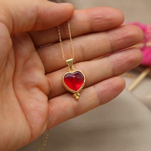 May include: A gold chain necklace with a red heart pendant. The heart is made of glass and has a gold trim.