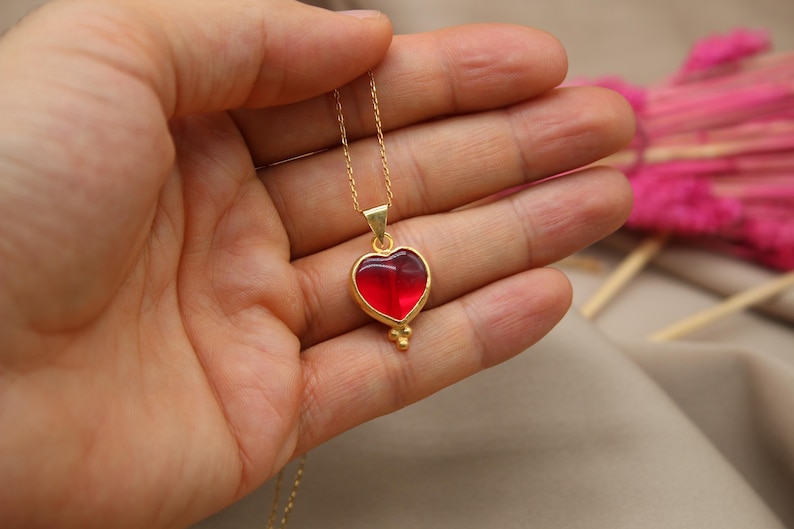May include: A gold chain necklace with a red heart pendant. The heart is made of glass and has a gold trim.