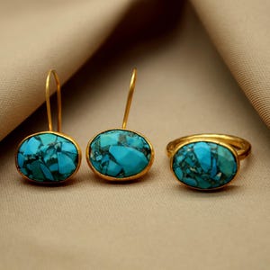 May include: A set of turquoise gemstone jewelry featuring a ring and a pair of earrings. The oval-shaped stones are set in gold.