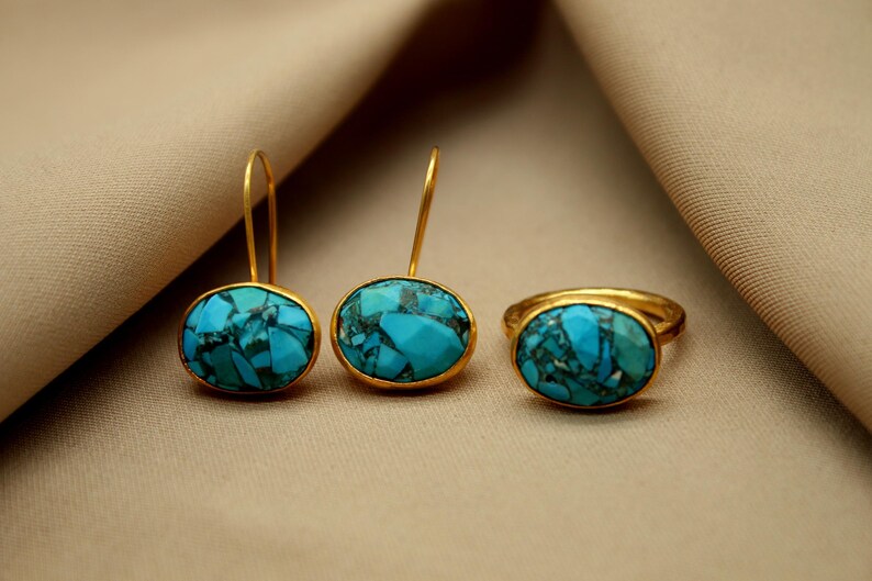 May include: A set of turquoise gemstone jewelry featuring a ring and a pair of earrings. The oval-shaped stones are set in gold.