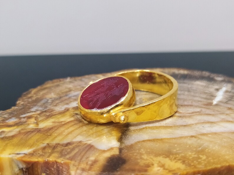 Peut inclure: Une bague en or avec une pierre pr&eacute;cieuse rouge sertie au centre. La bague a une texture martel&eacute;e et un design simple.