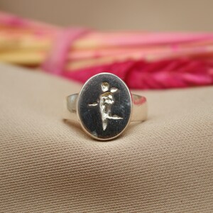 以下が含まれることがあります： 楕円形のセッティングに金のデザインが施された銀のリング。デザインは植物や花のスタイリッシュなイメージです。