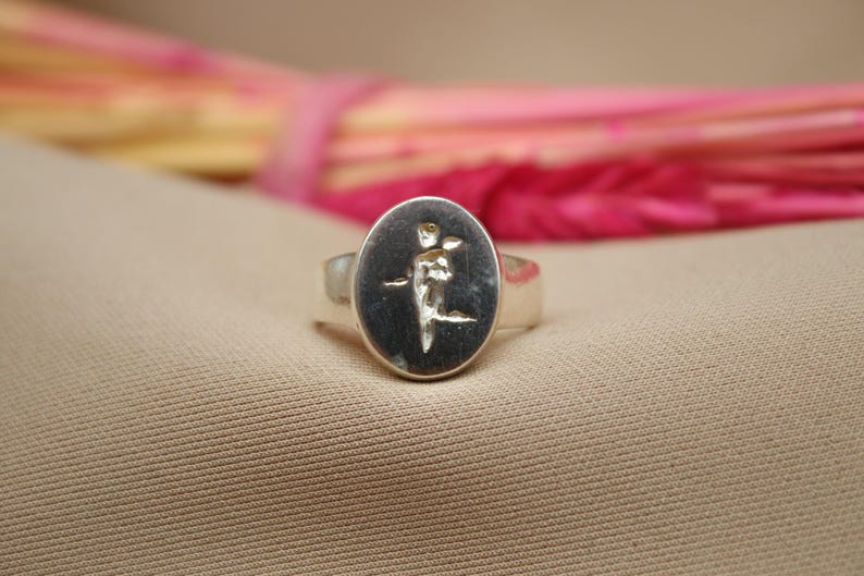 以下が含まれることがあります： 楕円形のセッティングに金のデザインが施された銀のリング。デザインは植物や花のスタイリッシュなイメージです。