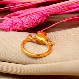 K&ouml;nnte beinhalten: Ein goldener Ring mit einem gro&szlig;en, runden, facettierten Edelstein. Der Ring hat eine strukturierte, geh&auml;mmerte Oberfl&auml;che und ein schlichtes, modernes Design.